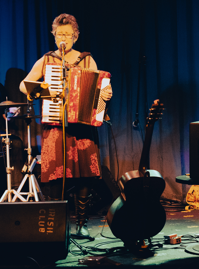 Queen Juanita plays the accordion while singing on stage.