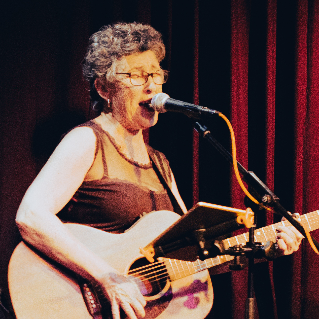 Queen Juanita singing and playing guitar live on stage.